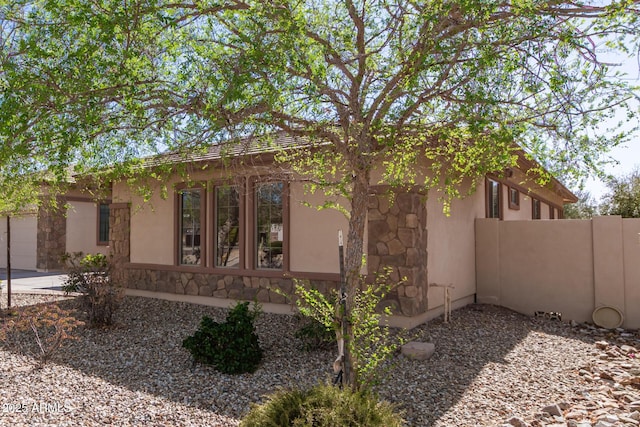 view of side of property featuring stone siding, fence, and stucco siding