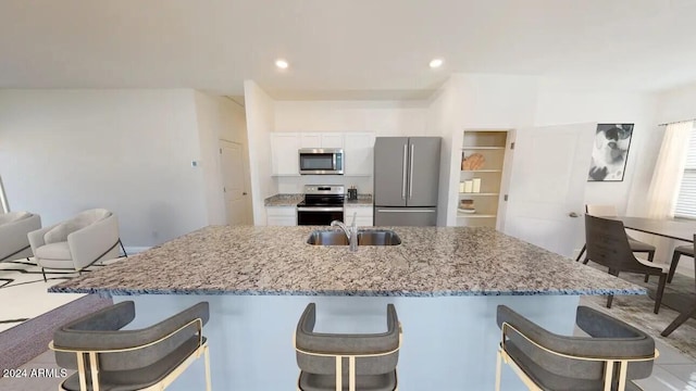 kitchen with stainless steel appliances, white cabinetry, sink, a breakfast bar, and light stone counters