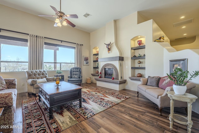 living room featuring lofted ceiling, dark wood-type flooring, ceiling fan, a large fireplace, and built in shelves