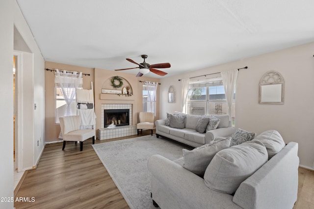 living room with a tile fireplace, ceiling fan, plenty of natural light, and light hardwood / wood-style flooring