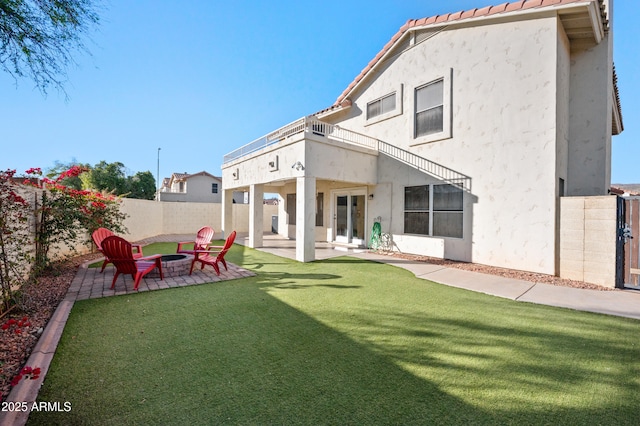 rear view of property featuring a yard, a patio area, a balcony, and a fire pit