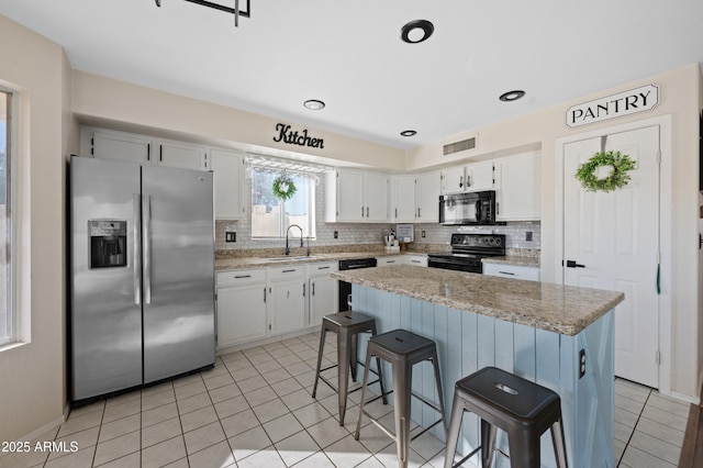 kitchen with black appliances, light stone counters, white cabinets, and sink