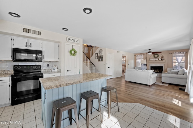 kitchen with a kitchen breakfast bar, tasteful backsplash, black appliances, light tile patterned floors, and white cabinets