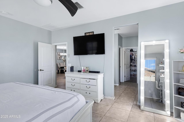 tiled bedroom with a spacious closet, ceiling fan with notable chandelier, and a closet