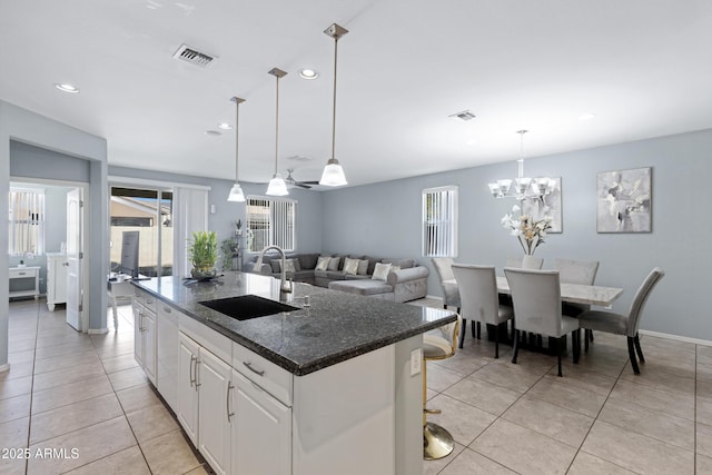 kitchen with a breakfast bar, pendant lighting, white cabinetry, sink, and a center island with sink