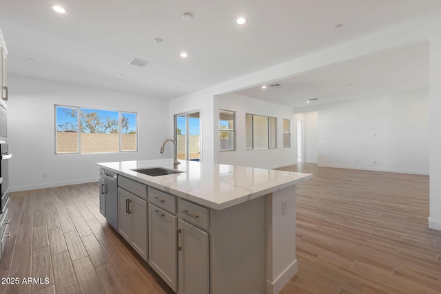 kitchen with light stone countertops, appliances with stainless steel finishes, a kitchen island with sink, sink, and gray cabinets