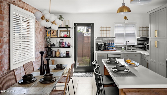 kitchen featuring sink, hanging light fixtures, brick wall, gray cabinets, and light tile patterned flooring