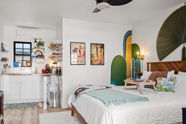 bedroom with a wall unit AC, ceiling fan, sink, and light wood-type flooring