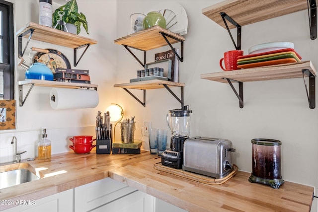 interior space with tasteful backsplash, white cabinetry, sink, and wooden counters