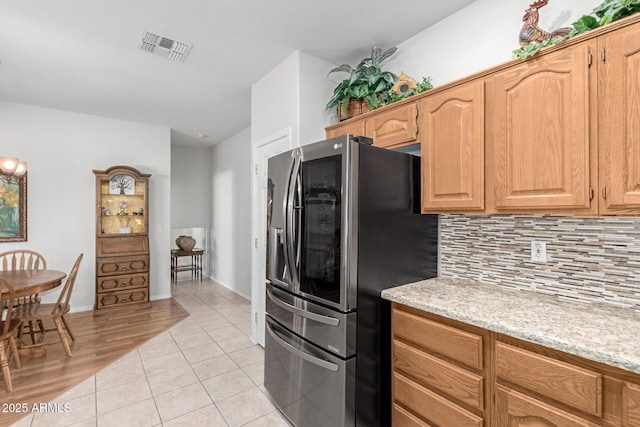 kitchen with light tile patterned flooring, light stone countertops, stainless steel refrigerator with ice dispenser, and tasteful backsplash