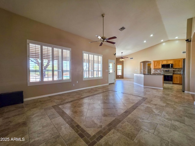 unfurnished living room with arched walkways, a ceiling fan, baseboards, a wealth of natural light, and visible vents