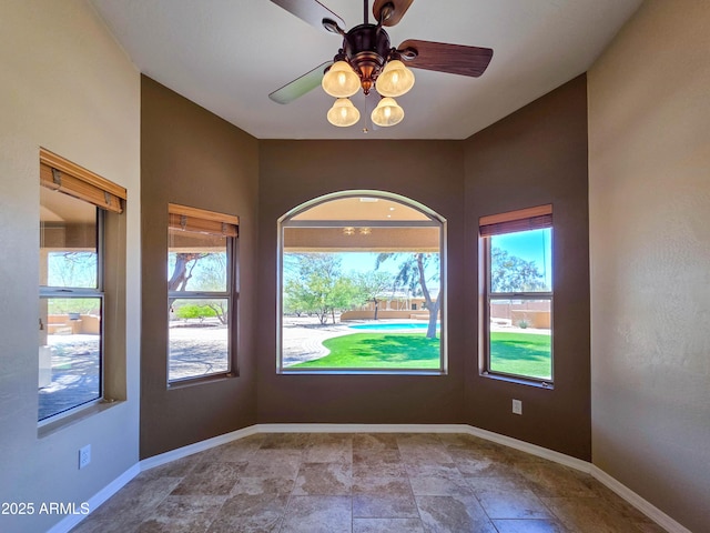 spare room featuring baseboards, a ceiling fan, and a wealth of natural light