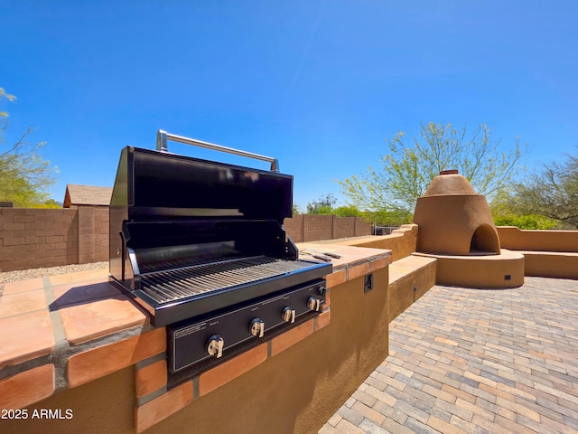 view of patio featuring an outdoor fireplace, exterior kitchen, area for grilling, and fence