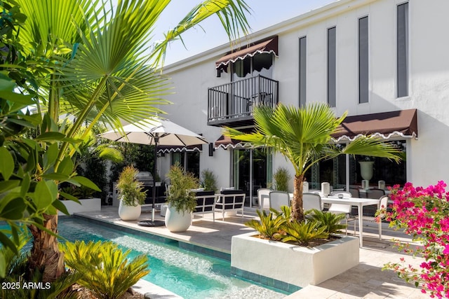 rear view of house featuring a patio, an outdoor pool, a balcony, and stucco siding