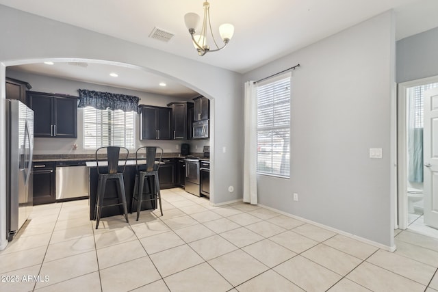 kitchen with light tile patterned flooring, appliances with stainless steel finishes, a center island, and a breakfast bar area