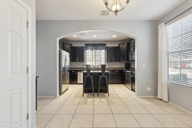 kitchen featuring light tile patterned floors, stainless steel appliances, a center island, and a kitchen bar