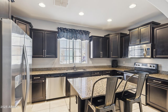 kitchen with appliances with stainless steel finishes, sink, a kitchen bar, a center island, and light tile patterned floors