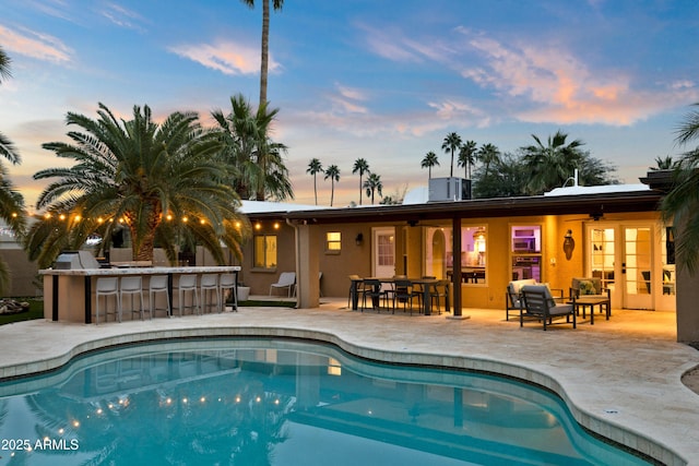 pool at dusk featuring a bar and a patio