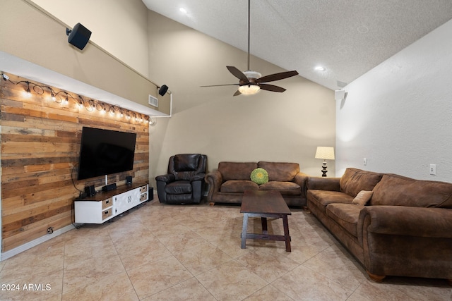 living room with a textured ceiling, high vaulted ceiling, ceiling fan, and wood walls