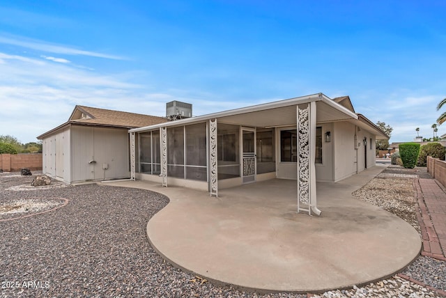 rear view of house featuring fence, a sunroom, a patio, and central AC