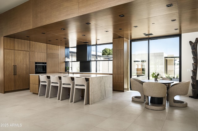 kitchen featuring light countertops, brown cabinetry, modern cabinets, a wall of windows, and oven