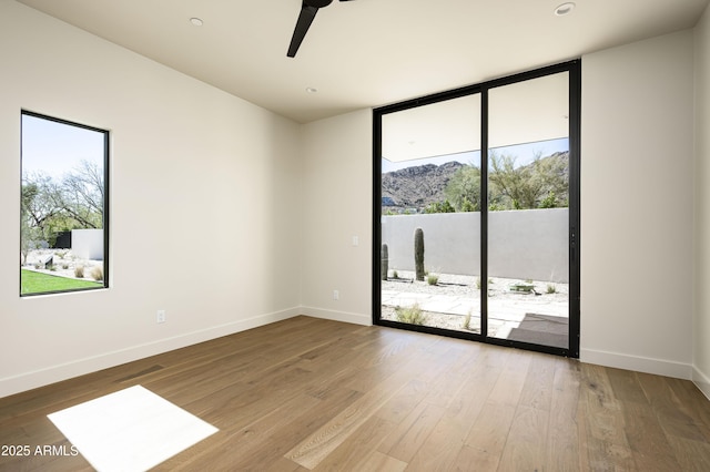 unfurnished room featuring a wall of windows, a ceiling fan, baseboards, and wood finished floors