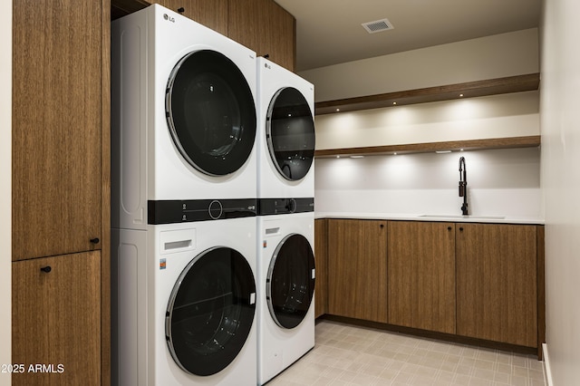 clothes washing area with cabinet space, visible vents, stacked washer and clothes dryer, light floors, and a sink