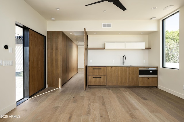 kitchen with a sink, visible vents, baseboards, brown cabinets, and light wood finished floors