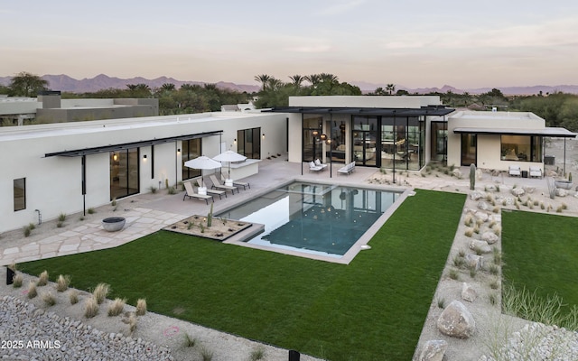 rear view of house with an outdoor pool, a patio area, a lawn, and a mountain view