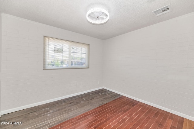 unfurnished room with dark hardwood / wood-style floors, a textured ceiling, and brick wall