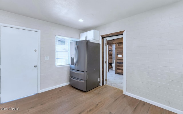 kitchen with stainless steel fridge, white cabinets, brick wall, and light wood-type flooring