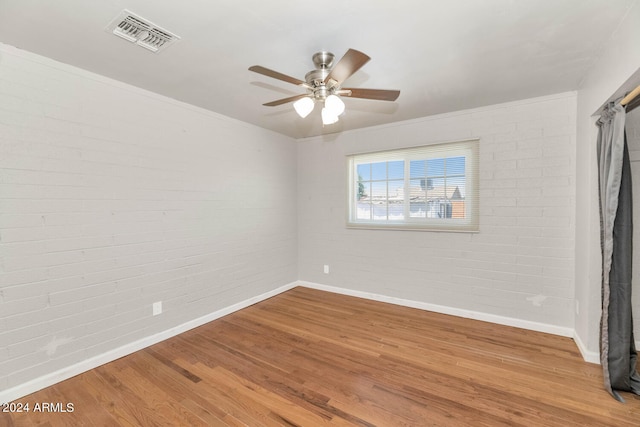 spare room with hardwood / wood-style flooring, ceiling fan, and brick wall