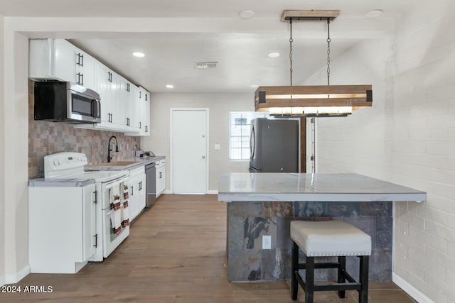 kitchen with appliances with stainless steel finishes, dark wood-type flooring, sink, white cabinets, and a breakfast bar area