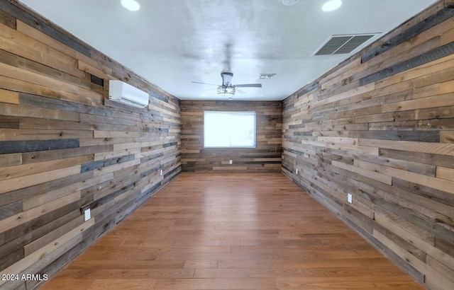 unfurnished room featuring a wall unit AC, wood walls, and hardwood / wood-style floors