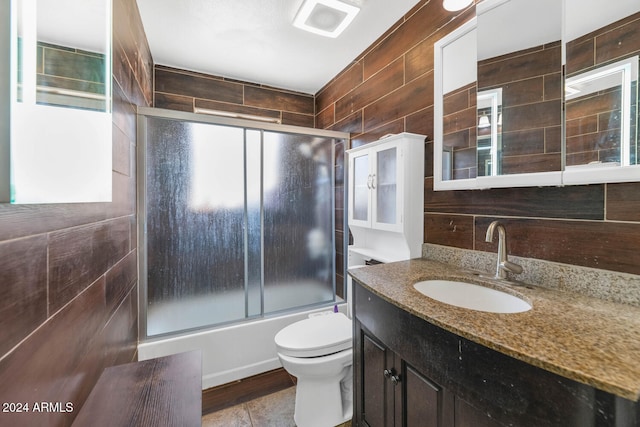 full bathroom with vanity, bath / shower combo with glass door, tile walls, and toilet