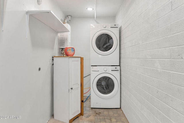 washroom featuring stacked washer / drying machine and brick wall