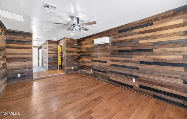 spare room with hardwood / wood-style flooring, an AC wall unit, ceiling fan, and wooden walls