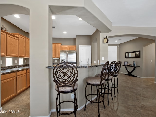 kitchen with a breakfast bar, stainless steel fridge with ice dispenser, and dark stone countertops