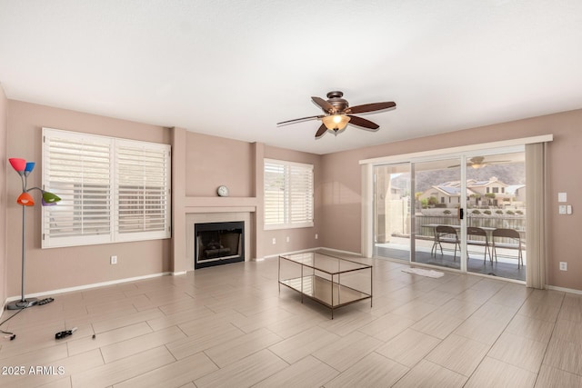 unfurnished living room with baseboards, a ceiling fan, and a fireplace