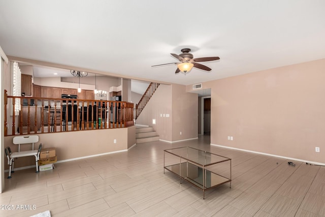 unfurnished living room featuring stairway, baseboards, ceiling fan with notable chandelier, and visible vents