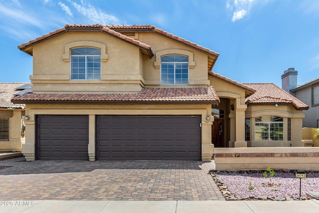mediterranean / spanish house with fence private yard, decorative driveway, stucco siding, a tiled roof, and an attached garage