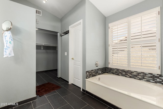 bathroom featuring a garden tub, baseboards, a walk in closet, tile patterned floors, and vaulted ceiling