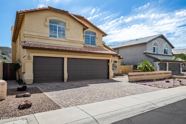 mediterranean / spanish-style home with a tile roof, a garage, decorative driveway, fence, and stucco siding