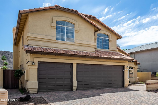 view of front of property with fence, decorative driveway, stucco siding, a tiled roof, and an attached garage