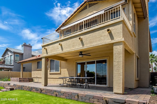 back of property featuring a ceiling fan, a patio area, fence, a balcony, and stucco siding