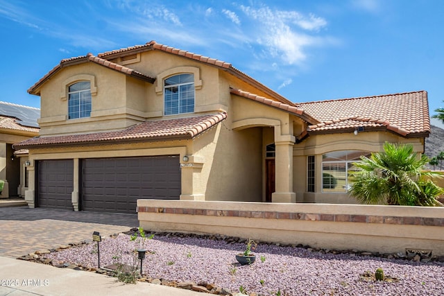 mediterranean / spanish-style house with decorative driveway, a garage, stucco siding, and a tile roof