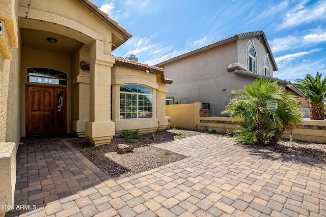 view of exterior entry featuring a patio, stucco siding, a tile roof, and fence