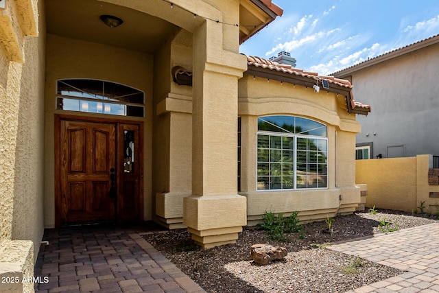 doorway to property with fence, stucco siding, and a tile roof