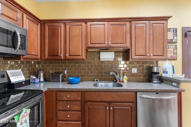 kitchen with light stone counters, decorative backsplash, brown cabinets, appliances with stainless steel finishes, and a sink