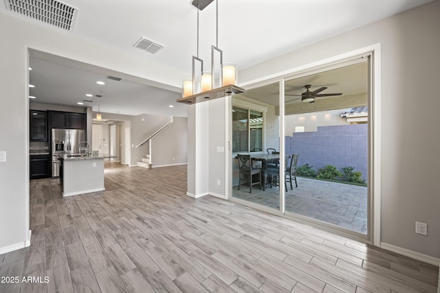 interior space with visible vents, a ceiling fan, light wood-style floors, and baseboards
